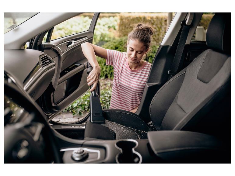 Frau saugt das Autointerieur mit einem Handstaubsauger.