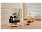 Cremefarbene Kaffeemaschine mit Kanne, daneben Kaffee, Milch und eine Tasse auf einer Holztheke.