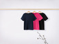 Drei T-Shirts, dunkelblau, rosa und schwarz, hängen an einer Holzstange.