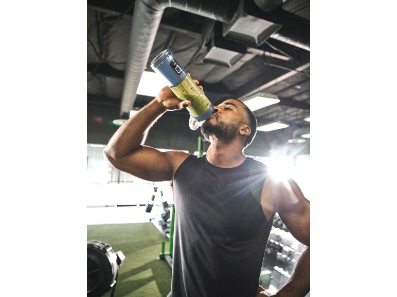 Mann trinkt grünen Smoothie aus tragbarem Mixer im Fitnessstudio.