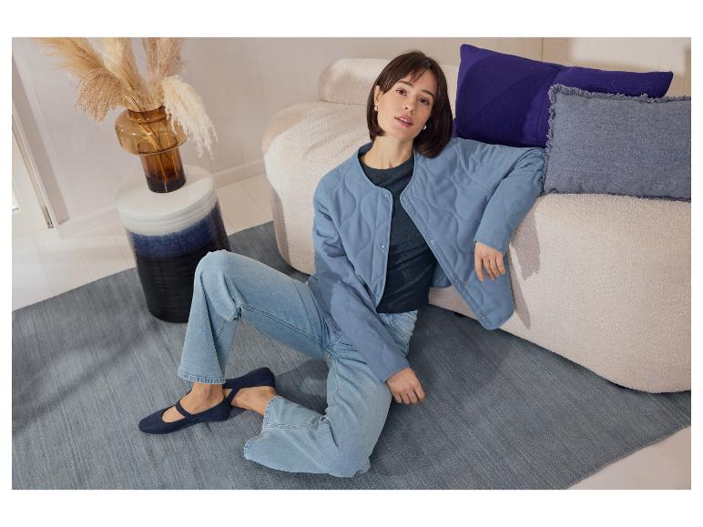 Frau in einer blauen ESMARA Steppjacke sitzt auf dem Boden neben einem Sofa.