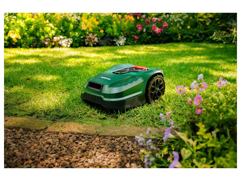 Ein grüner Mähroboter auf einem Rasen mit Blumen und Büschen im Hintergrund.