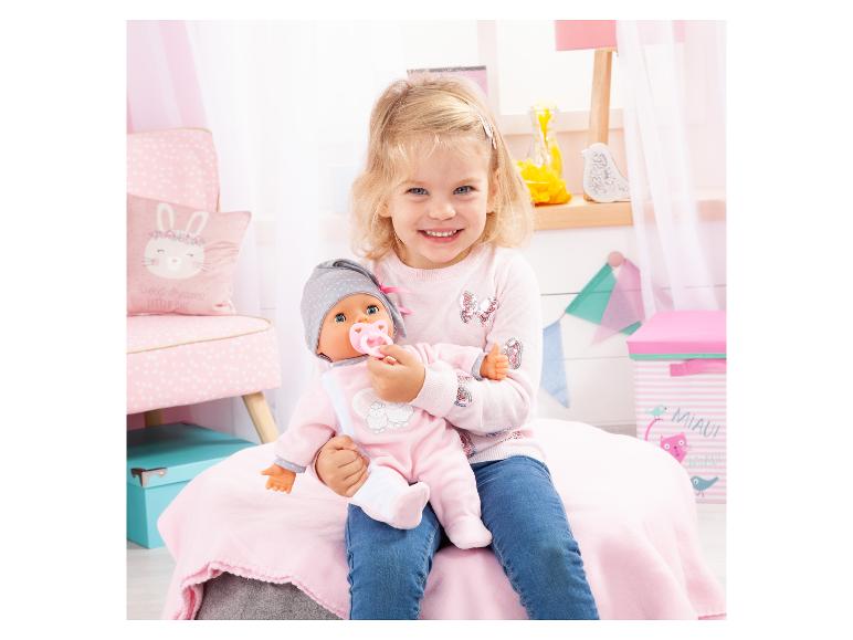 Lächelndes Mädchen hält eine Babypuppe mit Schnuller in einem rosa Zimmer.