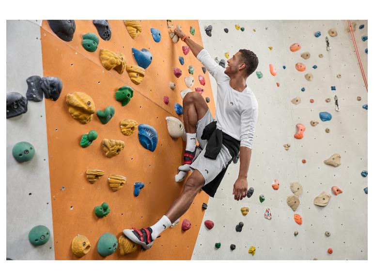 Mann in weißem Langarmshirt und grauen Shorts beim Indoor-Klettern