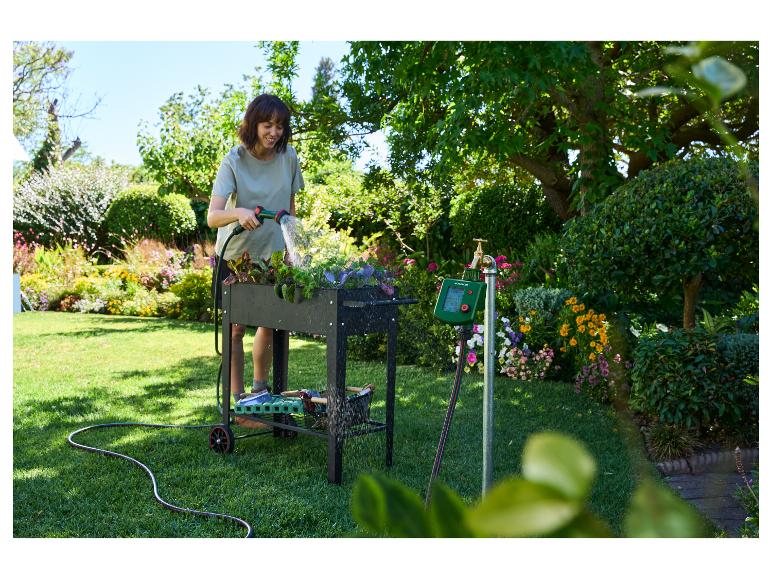 Frau bewässert Pflanzen im Hochbeet mit Bewässerungscomputer und Schlauch.
