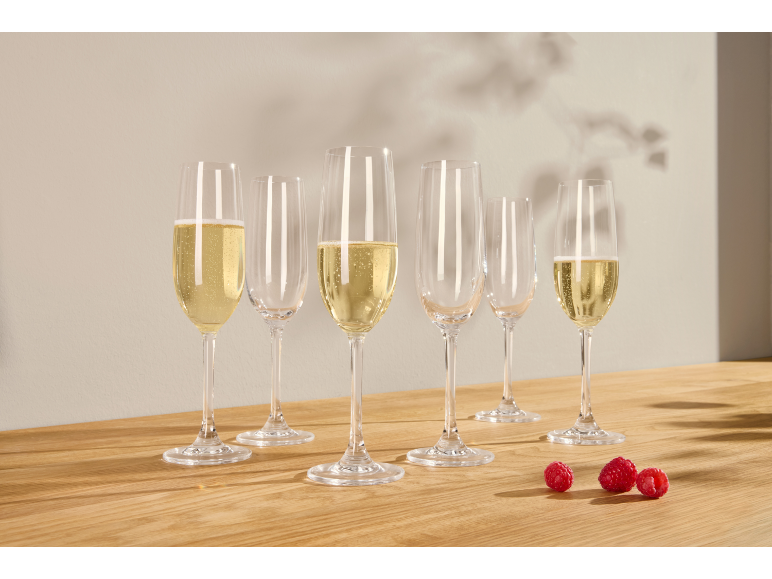 Sechs Sektgläser, einige mit Sekt gefüllt, und drei Himbeeren auf einem Holztisch.
