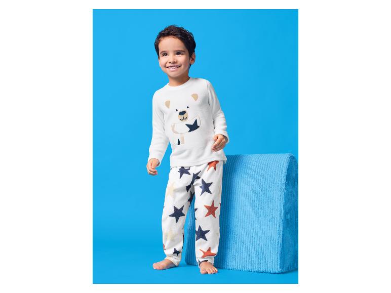 Glücklicher Junge in weißem Pyjama mit Bärenmotiv und Sternenmuster.