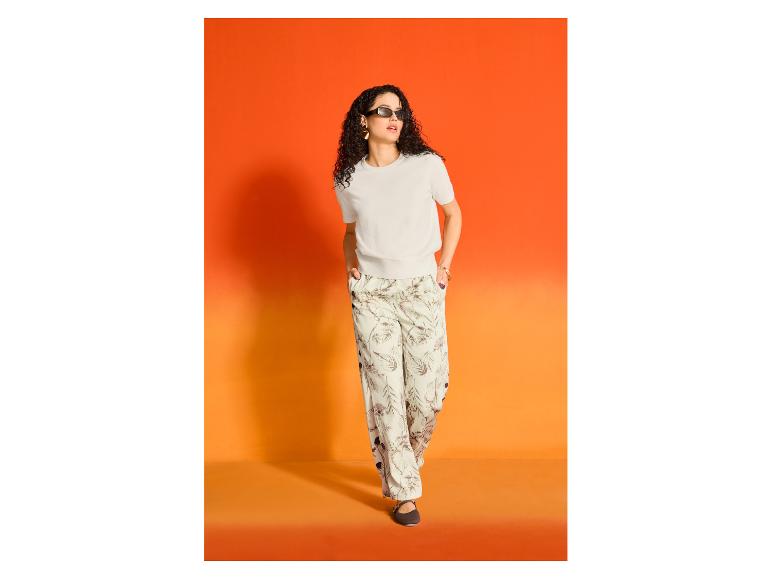 Frau in ESMARA® Wide-Leg-Hose und hellem T-Shirt vor orangefarbenem Hintergrund.