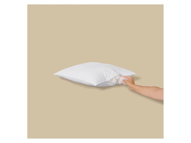 Eine Hand passt die Füllung eines weißen Kissens an und zeigt die weiche Füllung im Inneren.