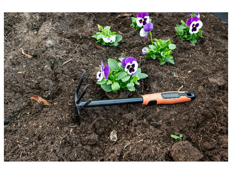 Lila Stiefmütterchen in der Erde neben einem orangefarbenen Gartengerät.
