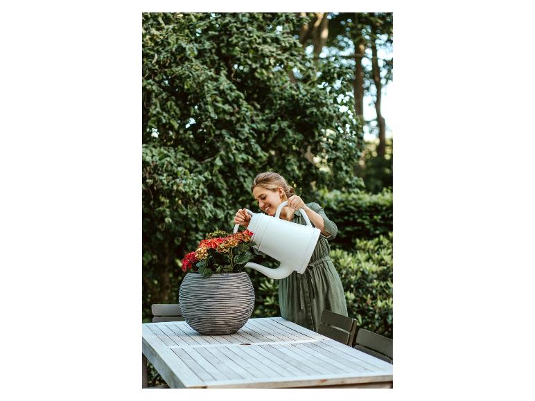 Frau gießt Blumen in einem Topf auf einem Holztisch im Garten.
