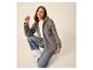 Frau in grauer Fleecejacke, weißem T-Shirt und blauen Jeans, hockend vor hellem Hintergrund.