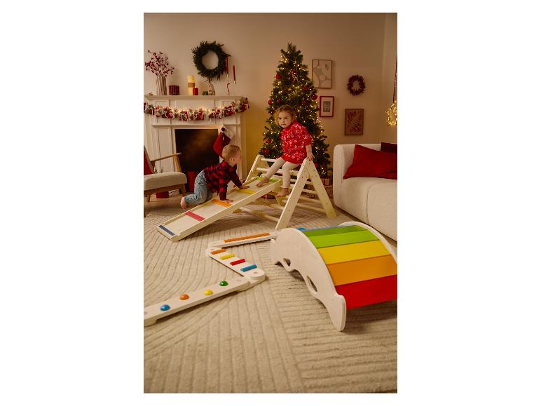 Zwei Kinder spielen mit Holzspielgeräten in einem weihnachtlich dekorierten Zimmer.