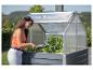 Frau gießt Pflanzen in einem Hochbeet mit Mini-Gewächshaus.
