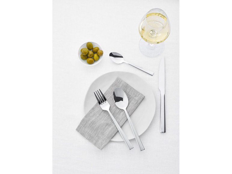 Ein gedeckter Tisch mit Besteck, einem Weinglas und Oliven.