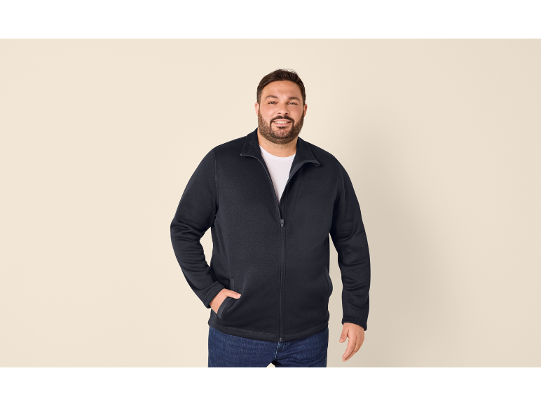 Lächelnder Mann in dunkelblauem Reißverschluss-Sweatshirt und Jeans.