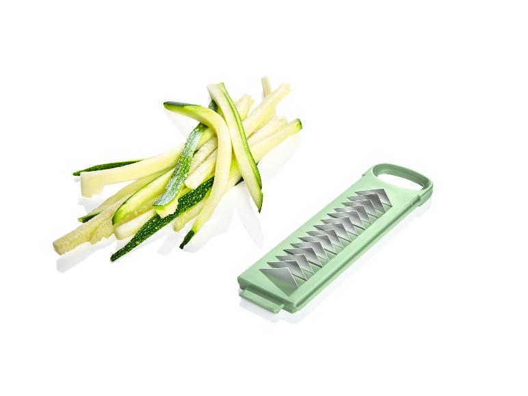 Grüne Zucchinistreifen und ein grüner Gemüseschäler auf weißem Hintergrund.