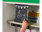 Kind zeichnet mit Kreide auf einer Spielküchentafel, neben Fruchtdarstellungen.