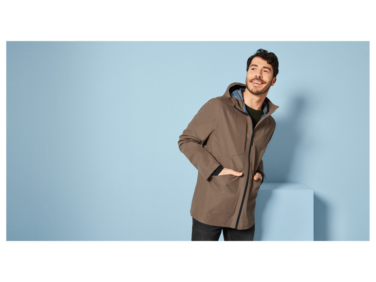 Mann in einer braunen Jacke mit Kapuze posiert vor einem blauen Hintergrund.