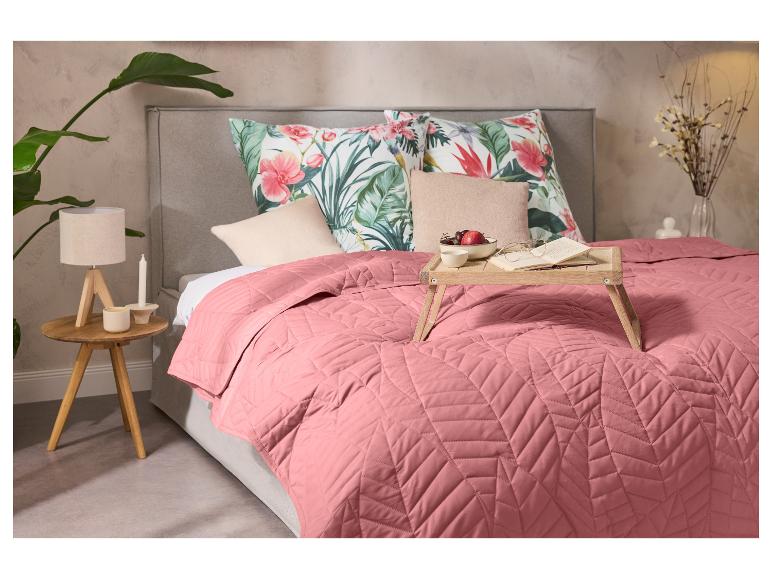 Schlafzimmer mit rosa Tagesdecke, Kissen mit Blumenmuster und einem hölzernen Frühstückstablett.