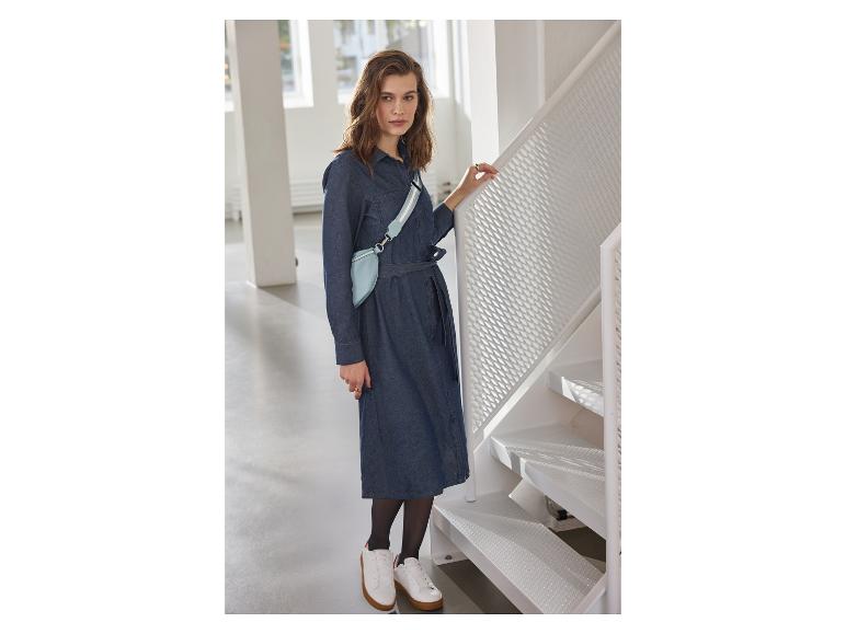 Frau in Jeanskleid, hellblauer Gürteltasche und weißen Sneakern an einer Treppe.