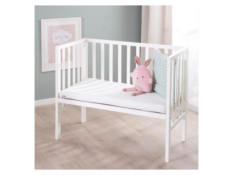 Weißes Babybett mit einem rosa Plüschtier und einem Kissen, neben einem Wolkenbild.