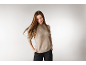 Eine Frau in einem beigen Strickpullover und einer schwarzen Hose posiert vor hellem Hintergrund