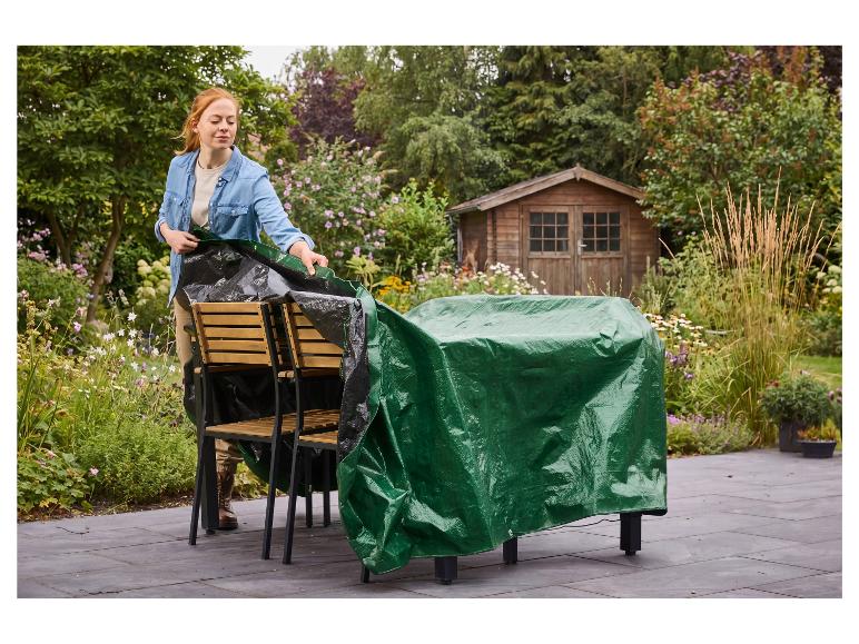 Eine Frau deckt Gartenmöbel mit einer grünen PARKSIDE Universal-Abdeckplane ab.