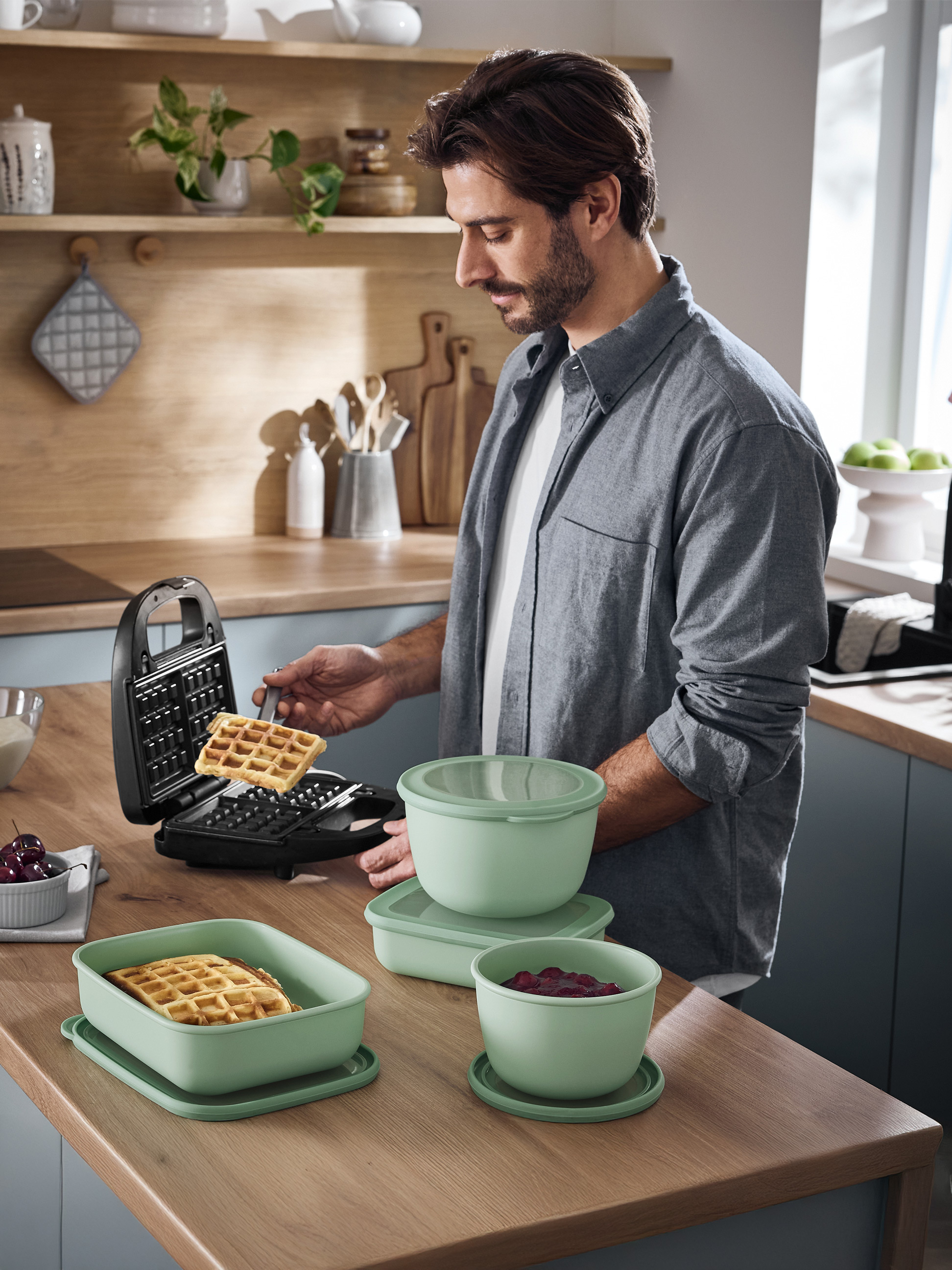 Mann bereitet Waffeln mit einem Waffeleisen zu und serviert sie in grünen Lebensmittelbehältern.