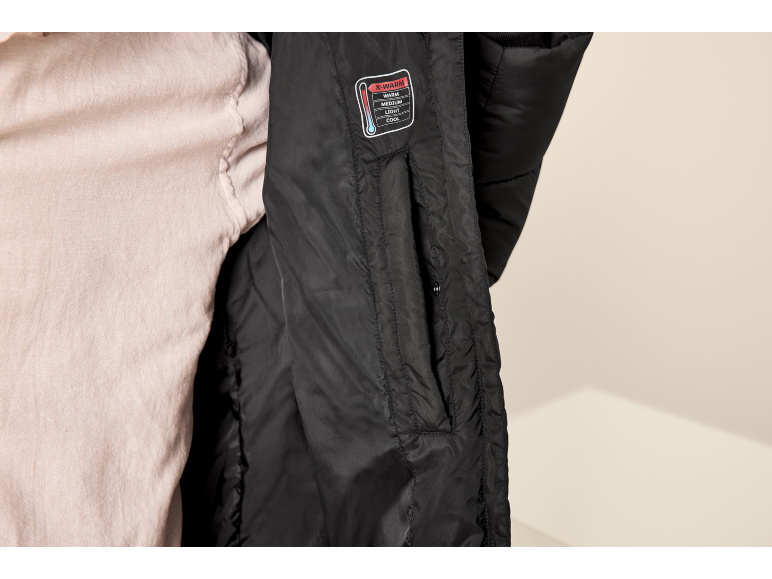 Innenseite einer schwarzen Steppjacke mit X-WARM Etikett und hellem T-Shirt.