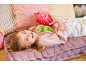Ein kleines Mädchen liegt auf einem rosa Kissen und hält ein Plüsch-Erdbeere.