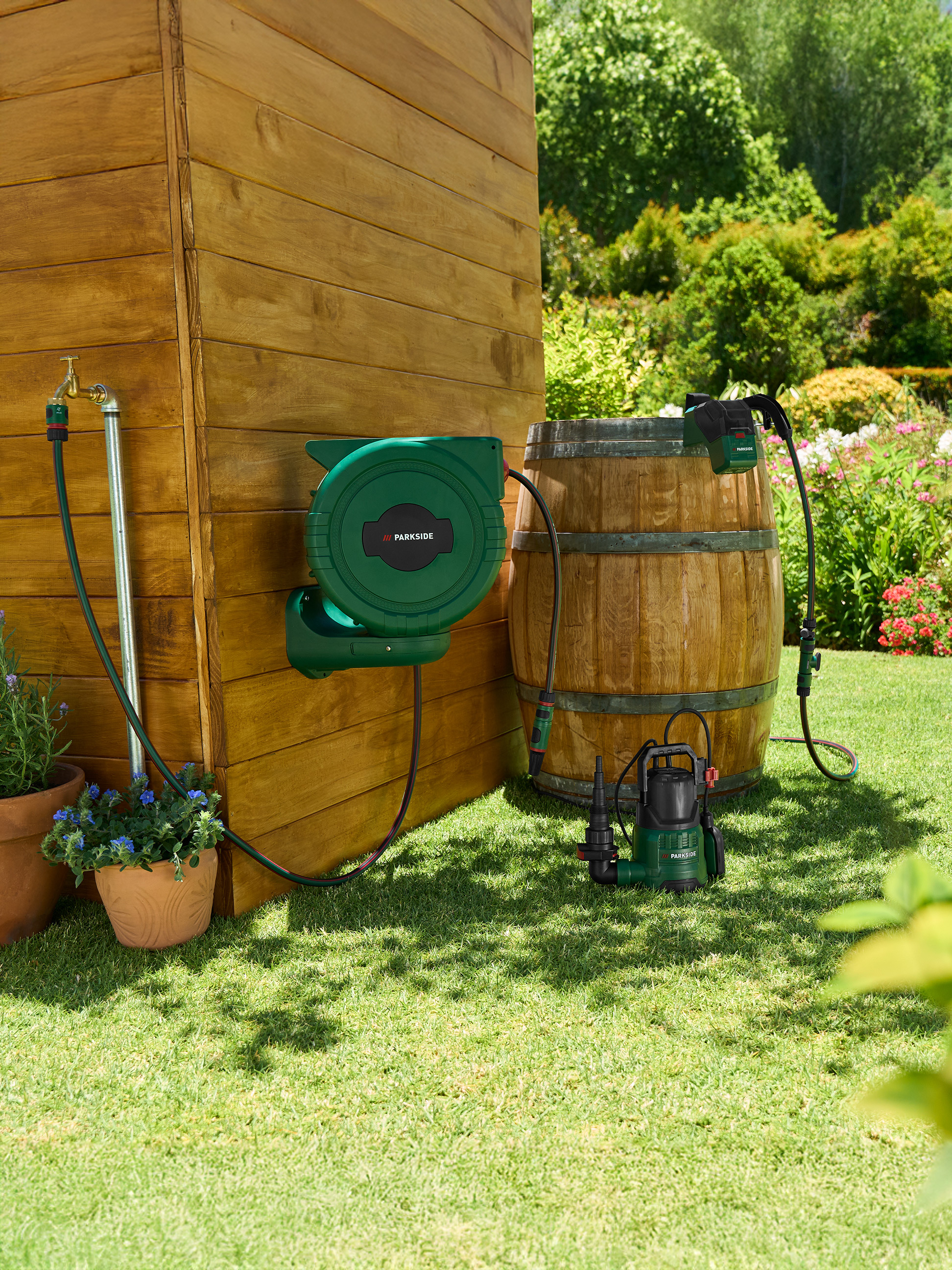 Gartenschlauchaufroller und Pumpe an einem Holzschuppen und Fass im Garten.