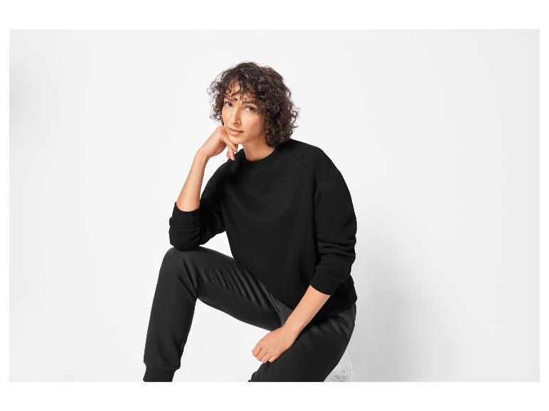 Eine Frau trägt einen schwarzen Pullover und eine schwarze Hose.