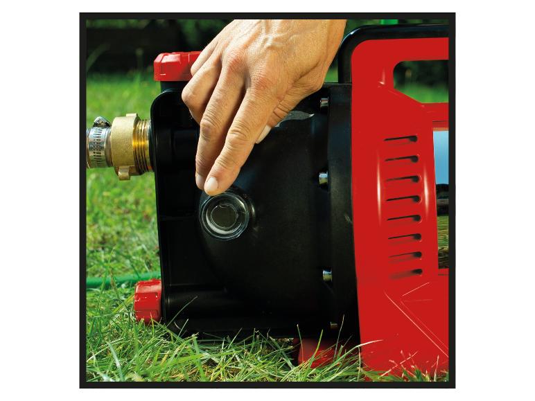Mann gießt Wasser in eine Pumpe auf einem Rasen.