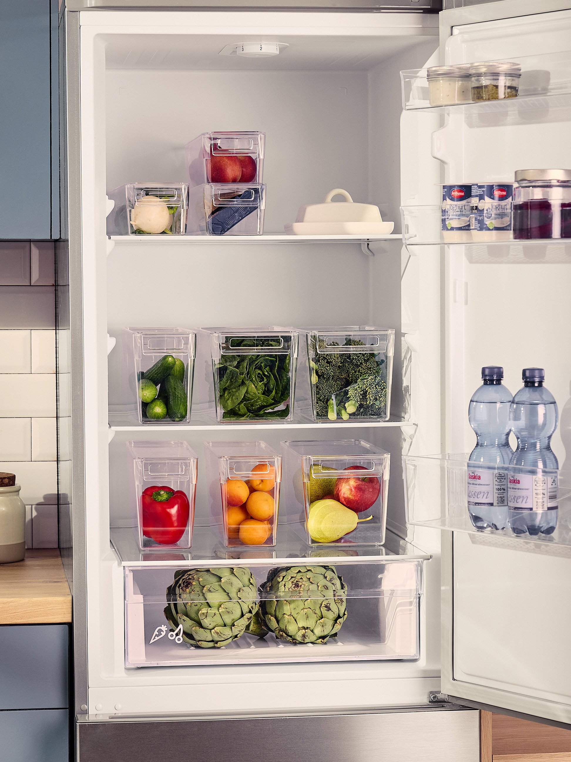 Offener Kühlschrank mit transparenten Behältern voller frischem Gemüse und Obst.