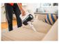 Person reinigt ein beiges Sofa mit einem weißen und schwarzen Handstaubsauger.