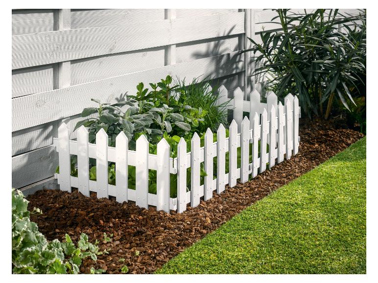 Weißer Zaun mit Pflanzen in einem Garten.