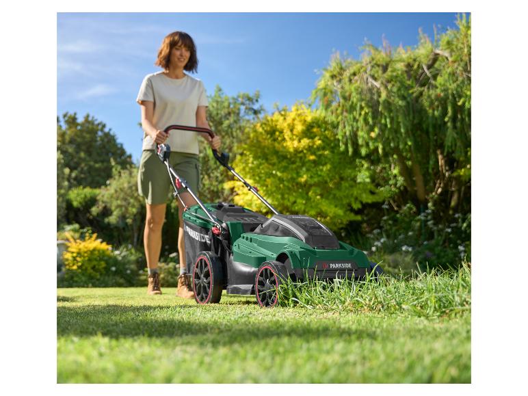 Eine Frau mäht einen sonnigen Rasen mit einem grün-schwarzen Rasenmäher.