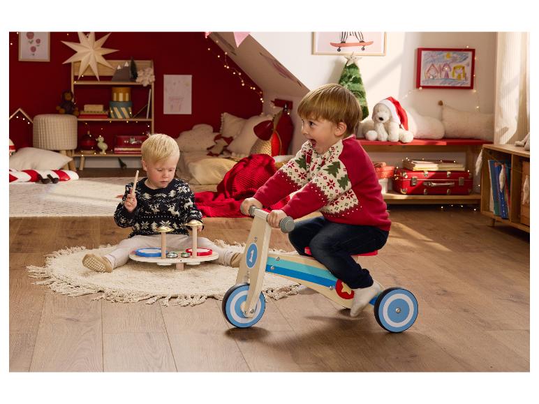 Zwei kleine Jungen spielen mit einem Laufrad aus Holz und einem Schlagzeug in einem festlichen Zimmer.