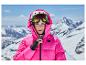 Frau in pinker Skijacke und Helm mit Skibrille vor verschneiter Bergkulisse.