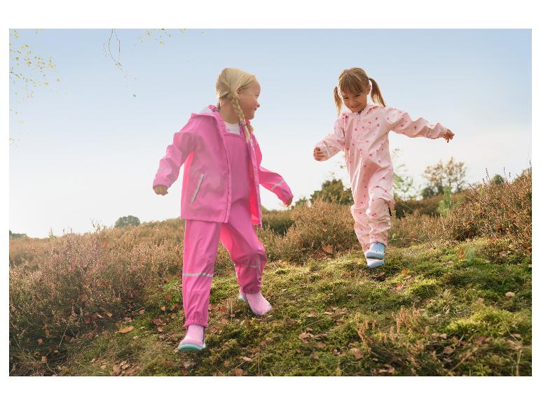 Zwei Mädchen in rosa Regenanzügen und Gummistiefeln spielen draußen.