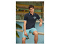 Mann in einem blauen Polo mit 'Surf Shop'-Logo und blauen Shorts.