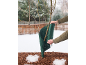 Person umwickelt Rosenstrauch mit grünem Winterschutz in einem verschneiten Garten.