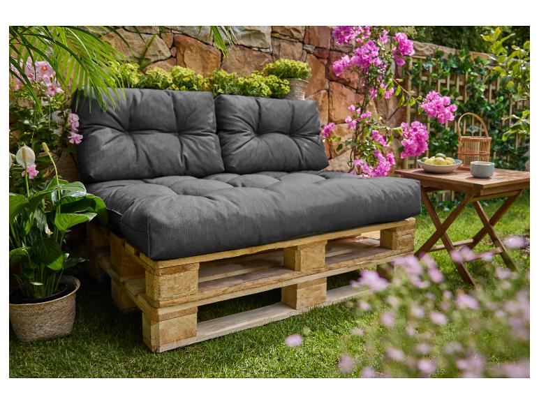 Outdoor-Palettensofa mit dunkelgrauen Kissen, umgeben von üppigem Grün und rosa Blüten.