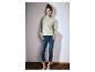 Frau in hellgrünem Sweatshirt mit Reißverschluss und hochgekrempelten blauen Jeans, steht an einer weißen Wand.