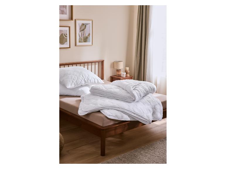 Weiße gesteppte Kissen und Bettdecke auf einem Holzbett in einem gemütlichen Schlafzimmer.