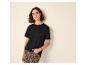 Frau in schwarzem T-Shirt und Leopardenhose, an eine Wand gelehnt.