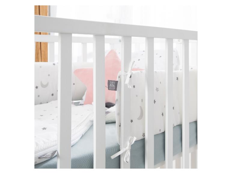 Babybett mit weißer Bettwäsche mit Sternen und Mond, und einem rosa Kissen.