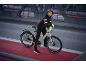 Frau in schwarzer Radsportbekleidung und gelben Handschuhen mit E-Bike auf einer Brücke.