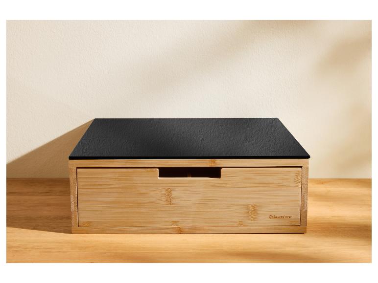 Ein Brotkasten aus Holz mit einem schwarzen schieferähnlichen Deckel auf einer Holzoberfläche.